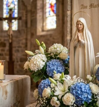Niewielka figurka Matki Boskiej w kościele otoczona jest kwiatami, świecami i różańcem. W tle, choć nieostry, widoczny jest Chrystus na krzyżu.