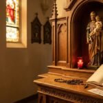 Obraz przedstawiający św. Józefa obok Jezusa wyrzeźbiony w drewnie wewnątrz kościoła, obok otwarta Biblia z tytułem artykułu