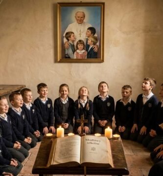 Zdjęcie grupy dzieci szkolnych siedzących i modlących się wokół Biblii, którą czyta ksiądz; w tle znajduje się zdjęcie Jana Pawła II z kilkoma dziećmi