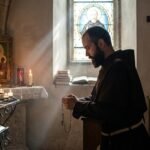 Obraz przedstawiający św. Maksymiliana jako młodego mężczyznę modlącego się z zamkniętymi oczami i klęczącego w kaplicy przed wizerunkiem Matki Boskiej i zapalonymi świecami