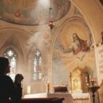 Sylwetka osoby modlącej się w kościele, na ołtarzu kościoła widnieje wizerunek Trójcy Świętej i Boga Ojca