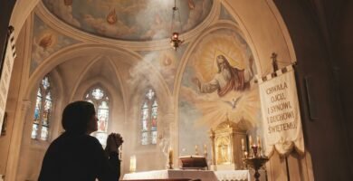 Sylwetka osoby modlącej się w kościele, na ołtarzu kościoła widnieje wizerunek Trójcy Świętej i Boga Ojca