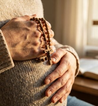 Zbliżenie na brzuch kobiety w ciąży z różańcem w dłoniach, w tle Biblia z krzyżem i świecą