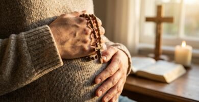 Zbliżenie na brzuch kobiety w ciąży z różańcem w dłoniach, w tle Biblia z krzyżem i świecą