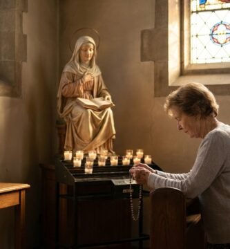 Imagen de una mujer mayor rezando con un rosario en las manos de rodillas frnete a la imagen de la virgen maria en el interior de una capilla