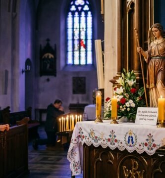 Obraz starszej kobiety modlącej się w kościele, przed nią znajduje się wizerunek archanioła Michała otoczony kwiatami i świecami